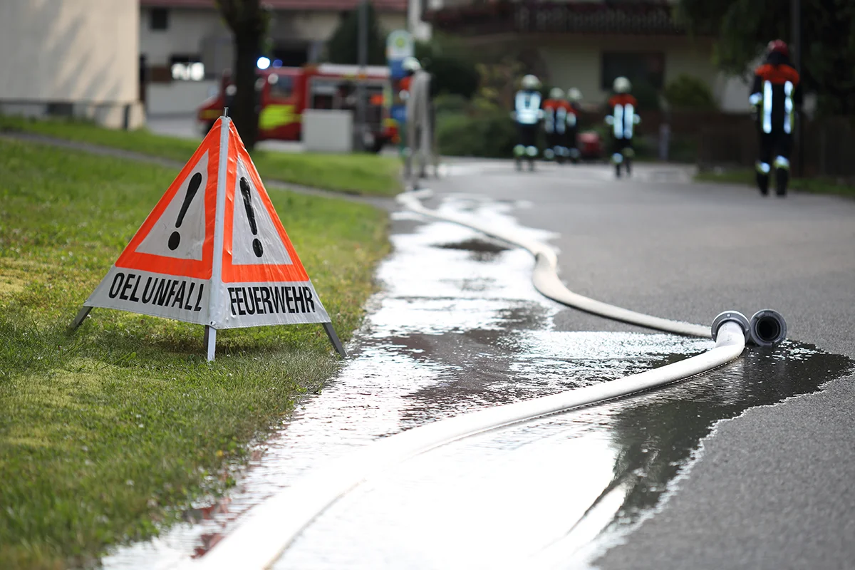 Eures • Feuerwehr im Einsatz, Warnschild und Wasserschlauch auf Straße.