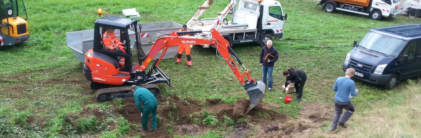 Eures • Baggerarbeiten auf einer Wiese mit mehreren anwesenden Personen.