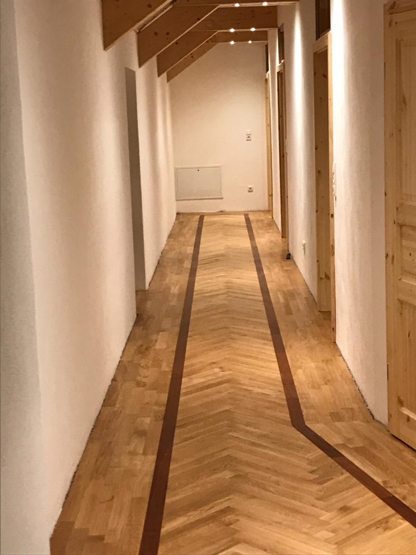 Eures • Holzfußboden in modernem Flur mit heller Wandgestaltung.