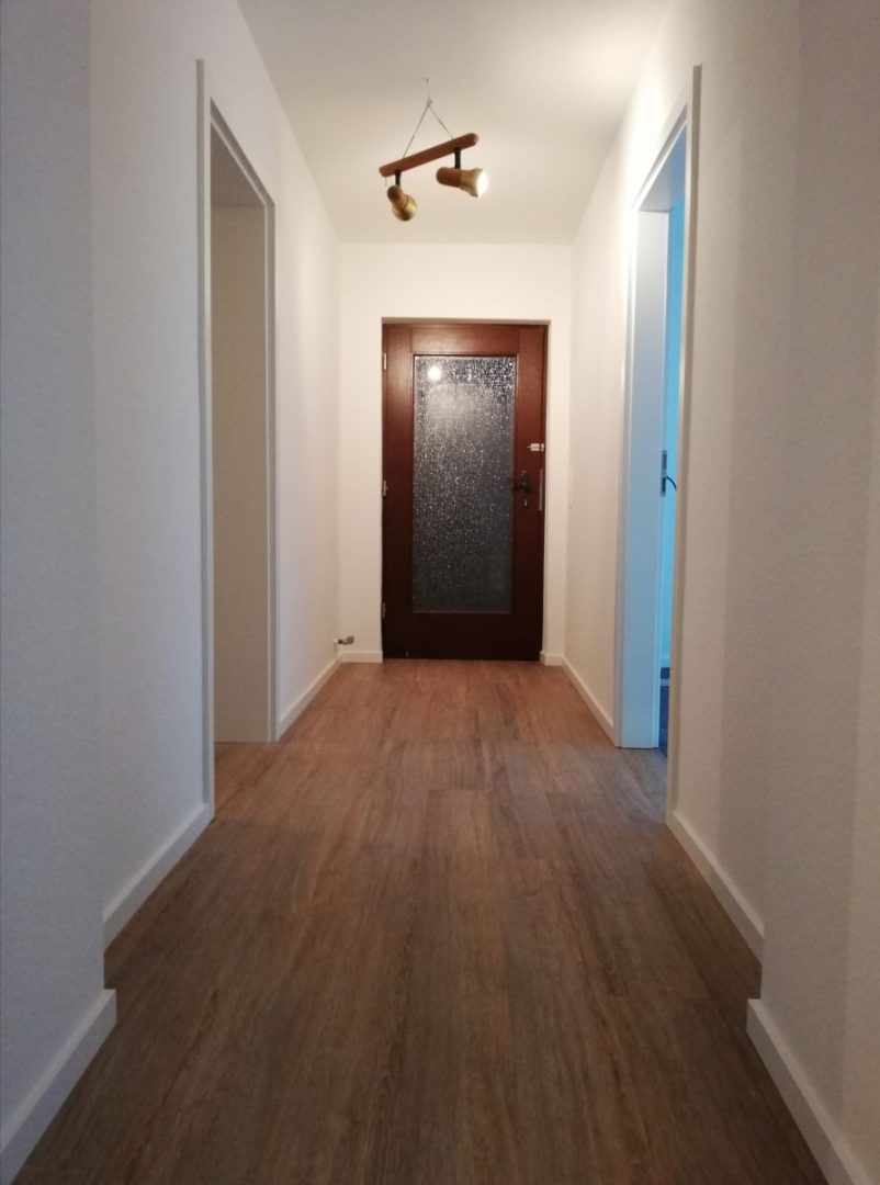 Eures • Heller Flur mit Holzfußboden und Eingangstür.