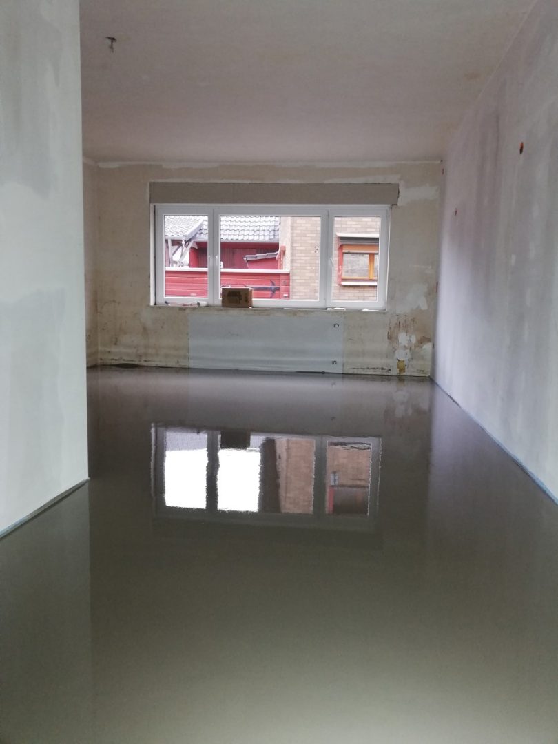 Eures • Frisch gegossener Fußboden in renoviertem Raum mit Fenstern.