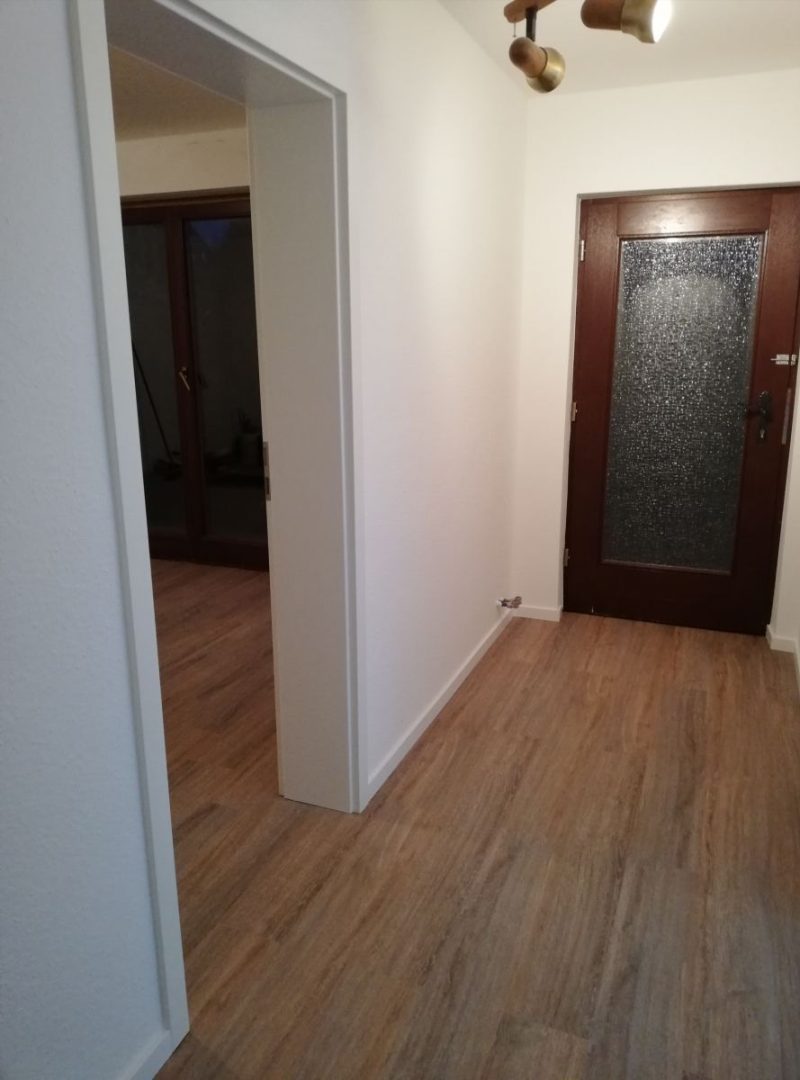 Eures • Heller Flur mit Holzfußboden und Glastür.