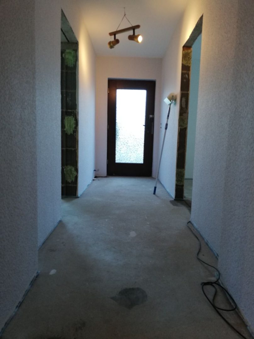 Eures • Heller Flur mit Eingangstür und Baustellenbeleuchtung.