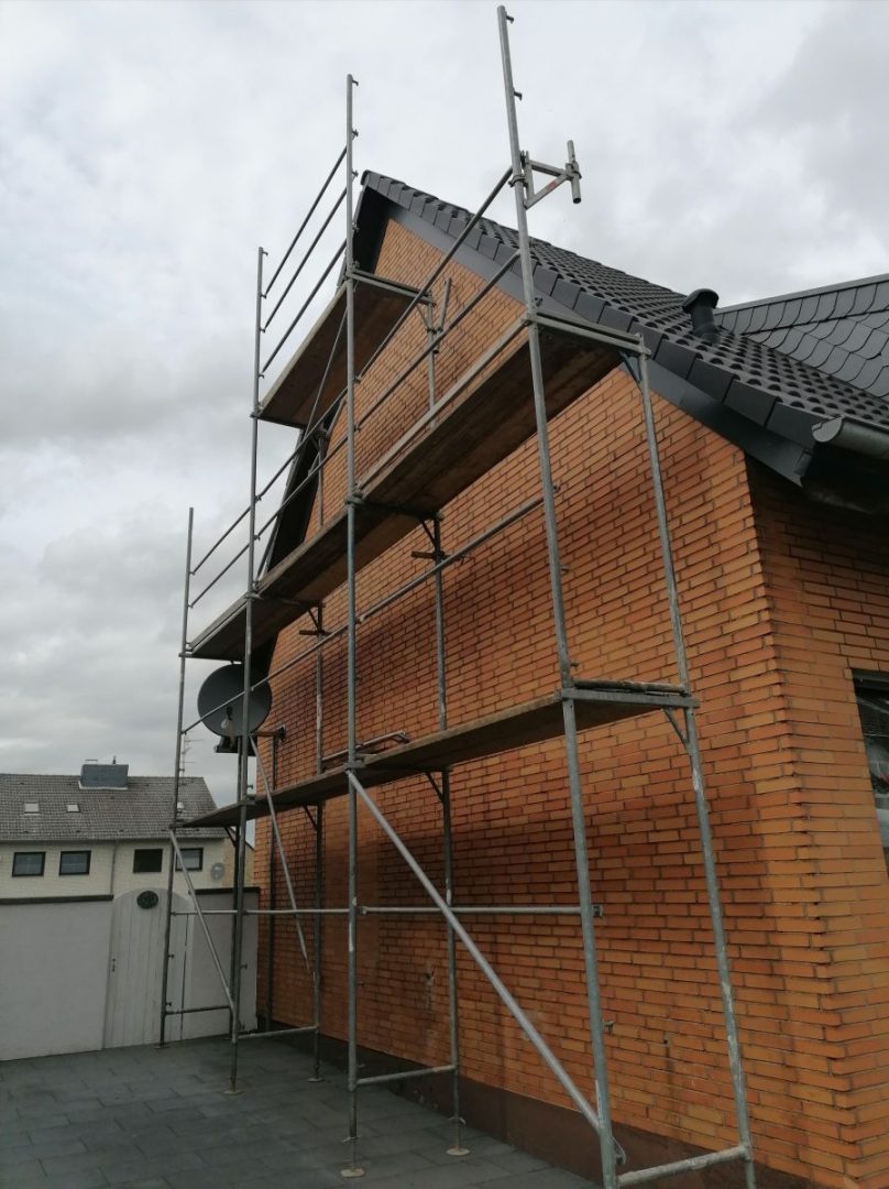 Eures • Gerüst an einem roten Ziegelhaus für Renovierungsarbeiten.