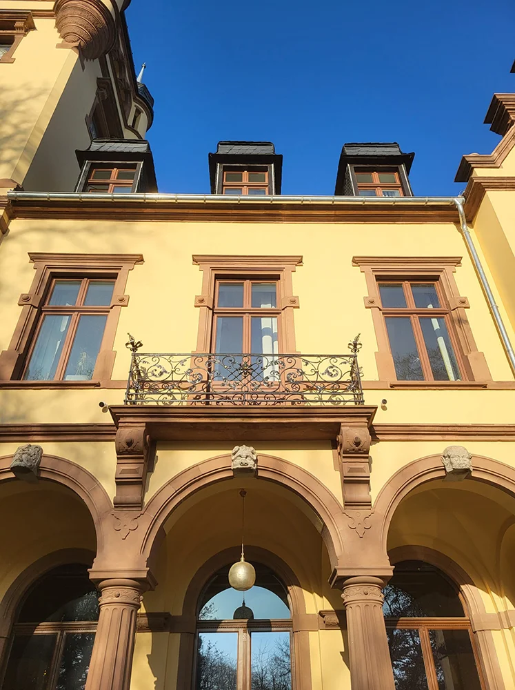 Eures • Historisches Gebäude mit gelber Fassade und Balkon im Freien.