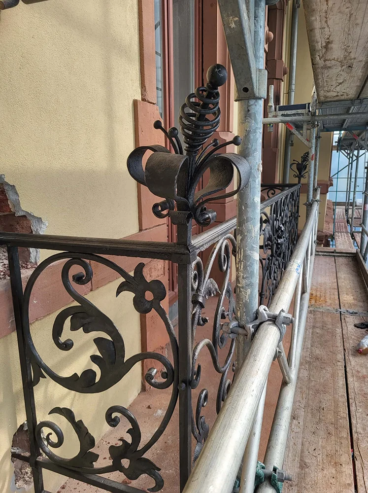 Eures • Schmiedeeisen-Balkongeländer mit kunstvollen Verzierungen und Baugerüst.