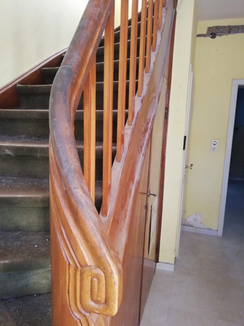 Eures • Holztreppe mit kunstvollem Geländer in einem Hausflur.