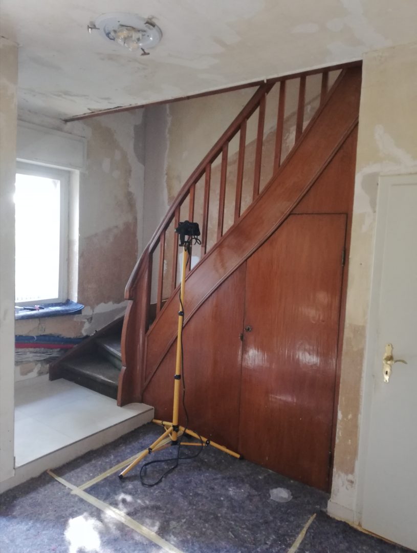 Eures • Renovierter Flur mit Holztreppe und Baustellenbeleuchtung.