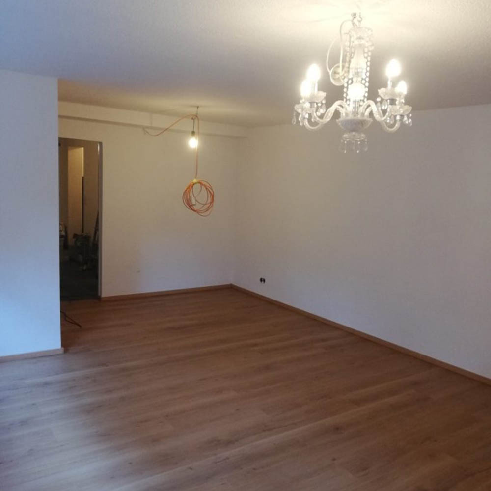 Eures • Leeres Wohnzimmer mit Holzfußboden und Kristalllüster.