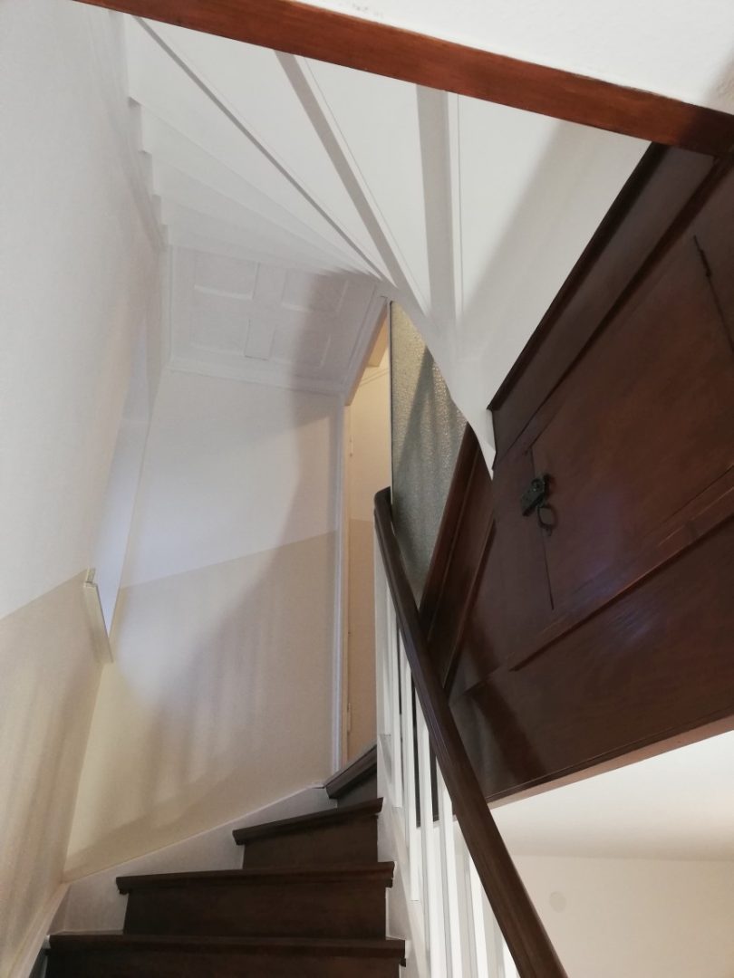Eures • Elegante Holztreppe mit weißen Wänden und verschlossenem Schrank.