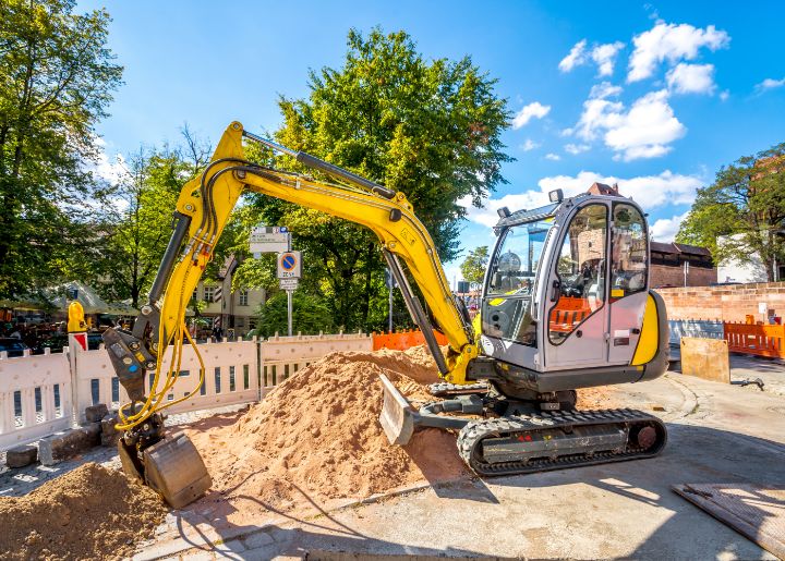 Eures • Gelber Bagger auf Baustelle mit Sandhügel und Baustellenabsperrung.